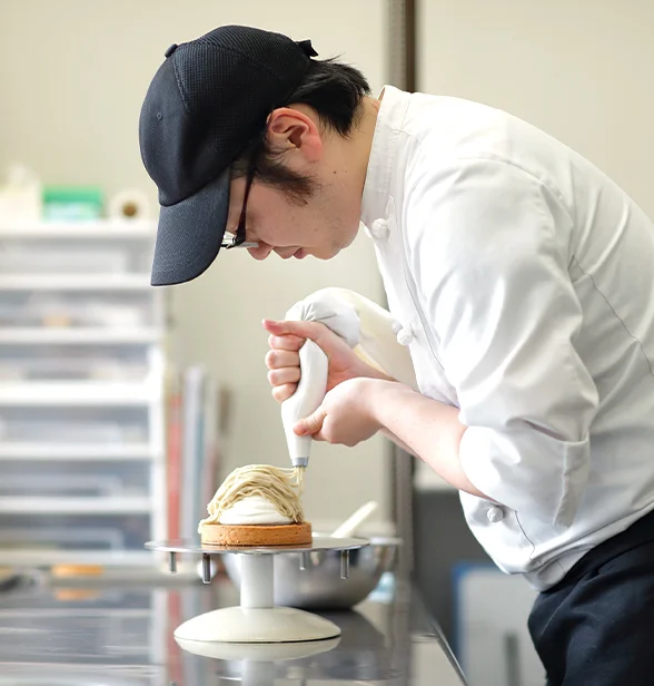 パティシエがケーキにクリームと果物を飾り付けている手元